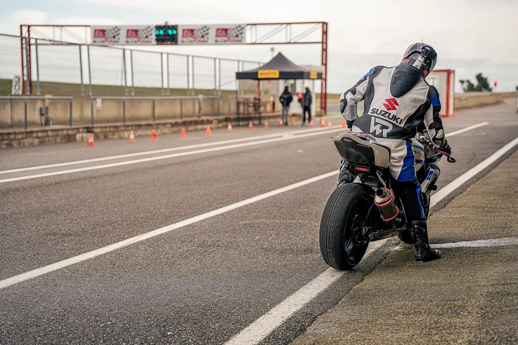 Pilota in moto in attesa all’uscita dei box, con il semaforo verde e i commissari sullo sfondo