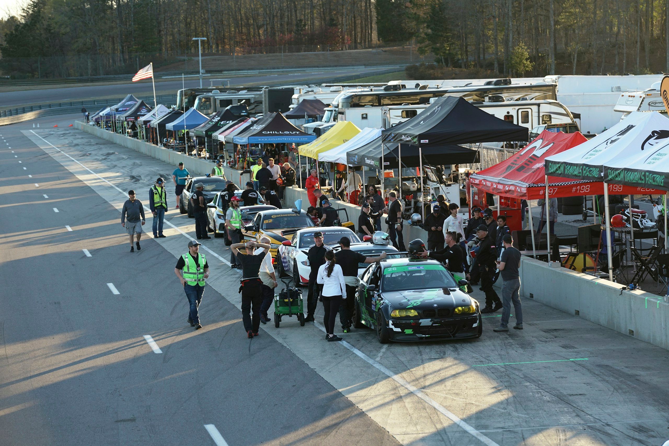 Pit lane at a track day with cars lined up, teams and marshals
